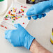A hand in a Showa blue biodegradable nitrile glove uses a knife to cut pills on a white tray.