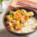 A bowl of stir fry with cubed tofu, rice, and vegetables.