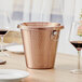 An Acopa copper spittoon on a table with wine glasses.