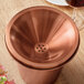 A copper Acopa wine tasting spittoon lid on a copper bucket with a glass of wine.