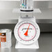 A white Cardinal Detecto mechanical portion scale with a red dial, weighing a can.