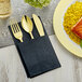 A black pocket fold dinner napkin with gold plastic cutlery in a napkin.