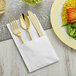 A Visions heavy weight gold plastic cutlery set with a white pocket fold dinner napkin including a fork, knife, and spoon.