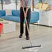A person using a Lavex double neoprene floor squeegee with a wooden handle to clean the floor.