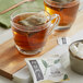 A glass mug of Numi Organic Hojicha tea with a tea bag on a wooden board.