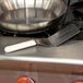 A pan with a Dexter-Russell solid turner with a white handle on a stove.