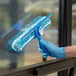 A hand in a blue glove cleaning a window with a Lavex squeegee and a blue sponge.