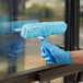 A hand in blue glove using a blue squeegee to clean a window.