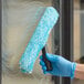 A person in blue gloves using a Lavex blue window cleaning sleeve on a window.