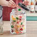 A person putting a lollipop into an Acopa Dusk glass jar filled with candy.