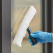 A hand in a blue glove using a white Lavex roller to clean a window.