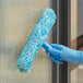 A hand in blue gloves using a blue and white fuzzy Lavex Pro strip washer sleeve to clean a window.