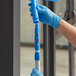 A person in blue gloves using a Lavex blue and silver Click / Lock Adapter Cone on a mop.