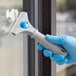 A hand in blue gloves using a Lavex scraper blade to clean a window.