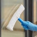 A hand in a blue glove using a Lavex strip washer to clean a window.