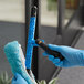 A person in blue gloves using a black and blue Lavex window cleaning tool.