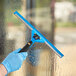 A person in blue gloves using a Lavex squeegee with a black handle to clean a window.