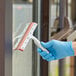 A hand in a blue glove using a Lavex 12" window squeegee to clean a window.