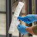 A person wearing blue gloves using a Lavex white fabric window cleaning sleeve to clean a window.