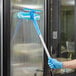 A person using a Lavex All-In-One window cleaning kit to clean a glass door while wearing blue gloves.