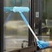 A person wearing blue gloves uses a Lavex All-In-One window mop to clean a window.