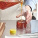 A hand pouring honey from a measuring device into a yellow plastic honey bottle.