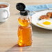 A honey bear bottle with a black lid on a table next to eggs and toast.