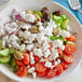 A bowl of Greek salad with tomatoes, olives, and Violife Just Like Greek Feta vegan cheese.