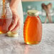 A person pouring honey into a Classic Queenline glass honey jar.
