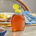 A Classic Queenline PET honey bottle with a yellow plastic flip top lid on a table.