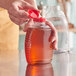 A hand pouring honey into a Queenline PET honey bottle with a red cap.