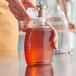 A close-up of a person pouring honey into a Queenline PET honey bottle with a white cap.