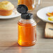 A bottle of honey with a black cap on a table near a muffin.