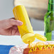 A hand holding a yellow bottle squeezing mustard onto a hot dog.