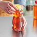 A person pouring honey into a bear-shaped PET honey bottle with a yellow cap.