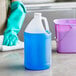 A translucent HDPE jug filled with blue cleaning liquid with a white cap next to a blue bucket and gloves.