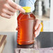 A hand holding a Ribbed Hourglass PET Honey Bottle filled with honey over a wood surface.