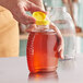 A person pouring honey into a Queenline PET honey bottle on a kitchen counter.