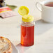 A 5.5 oz. clear cylinder sauce bottle with a yellow cap filled with brown liquid on a table.