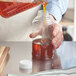 A person pouring honey into a container using a Skep PET sauce bottle.