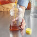 A person pouring honey into a Ribbed Hourglass PET plastic bottle.