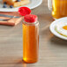 A 8 oz. clear PET sauce bottle of honey with a red cap.