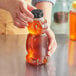 A hand holding a 16 oz. bear-shaped plastic bottle of honey with a black cap.