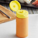 A 5.5 oz. clear plastic cylinder sauce bottle with a yellow inverted squeeze bottle lid.