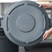 A person holding a Rubbermaid grey round trash can lid.