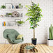 An artificial ficus tree in a black metal planter in a room with a green chair and bookshelf.