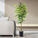 A LCG Sales artificial ficus tree in a black metal planter in front of a white couch.