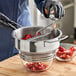 A person in a blue uniform using a Choice Prep stainless steel rotary food mill to process strawberries.
