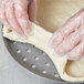 A person in plastic gloves using an American Metalcraft Super Perforated Hard Coat Anodized Aluminum Cutter Pizza Pan to make dough.