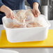 A person putting a bag of chicken in a white Choice plastic food storage container.